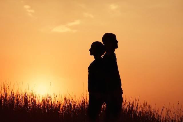 silhouette of man and woman standing in field of grass